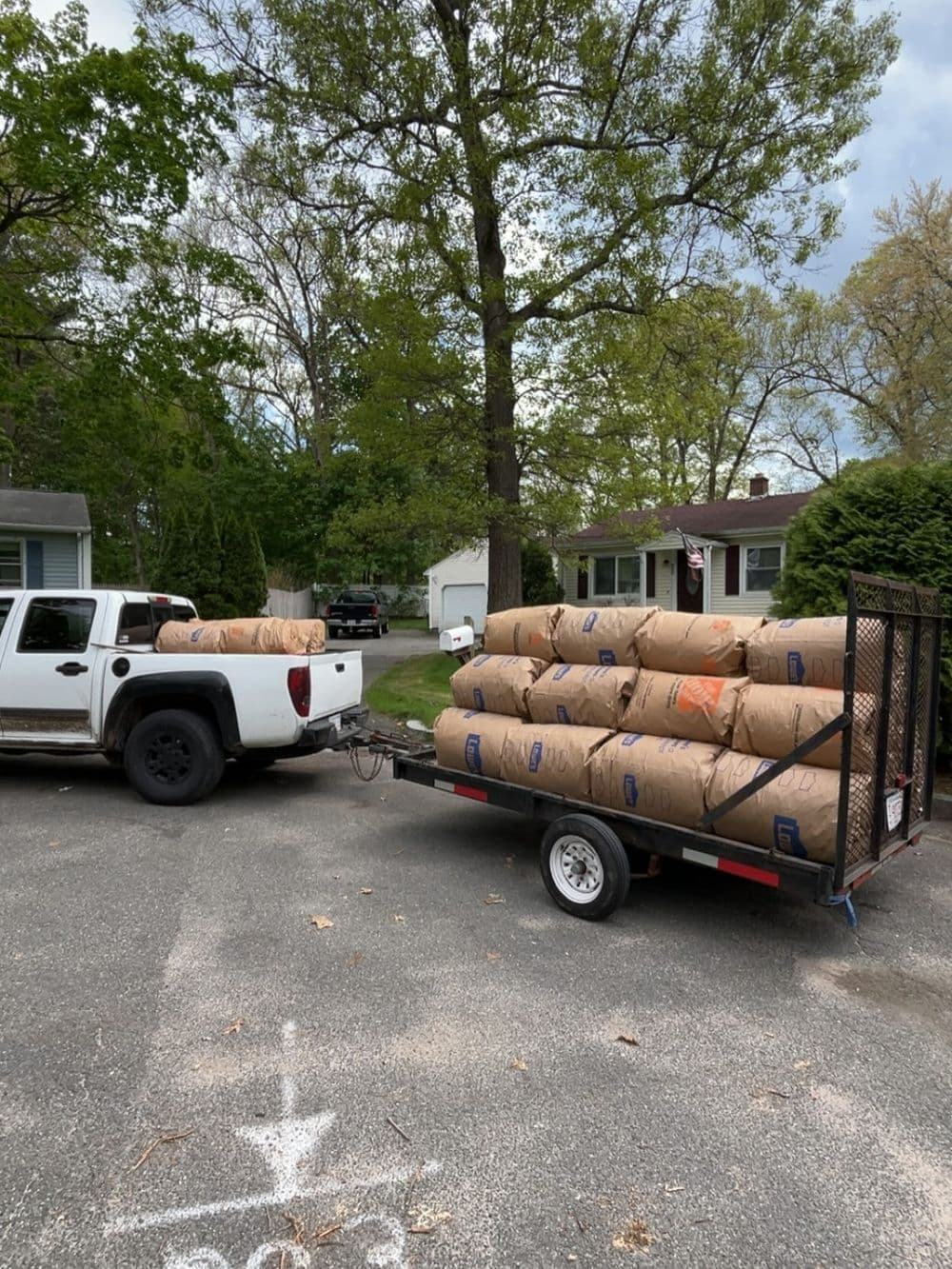 Pickup truck towing a trailer loaded with large bags in a residential neighborhood.
