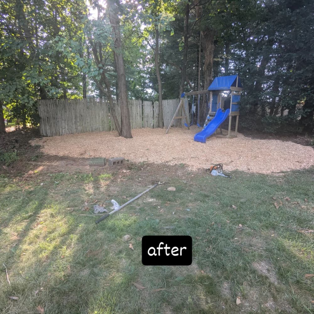 Playground renovation with fresh wood chips and slide in a backyard setting surrounded by trees.
